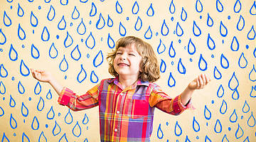 Child in front of blue water drops, raising the arms as if it welcomes rain.
