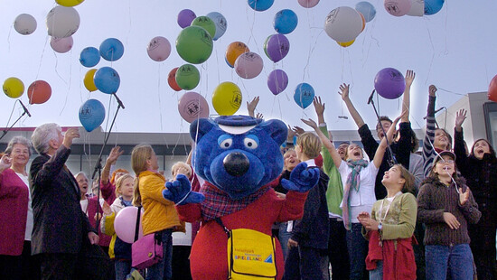 Ansicht einer Menschengruppe, mit Luftballons und eine Figur im Kostüm von Käptn Blaubär