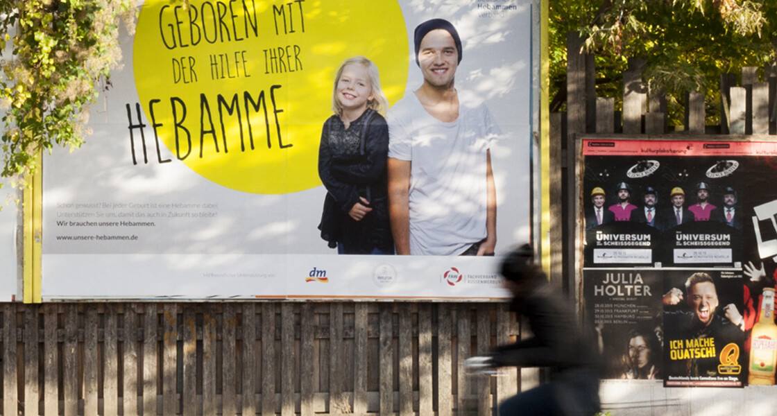 big poster showing two kids "born with the help of their midwife" at the countryside