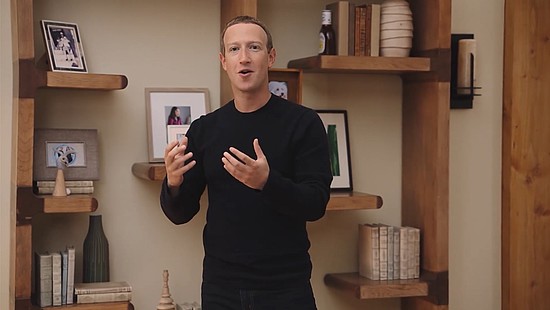 Mark Zuckerberg all in black in front of a beige wall with small bookshelves