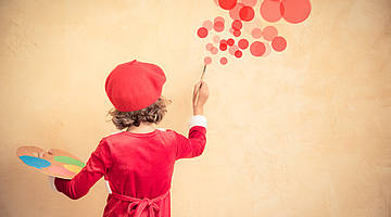 Kind mit roter Baskenmütze, rote Kreise an eine Wand malend