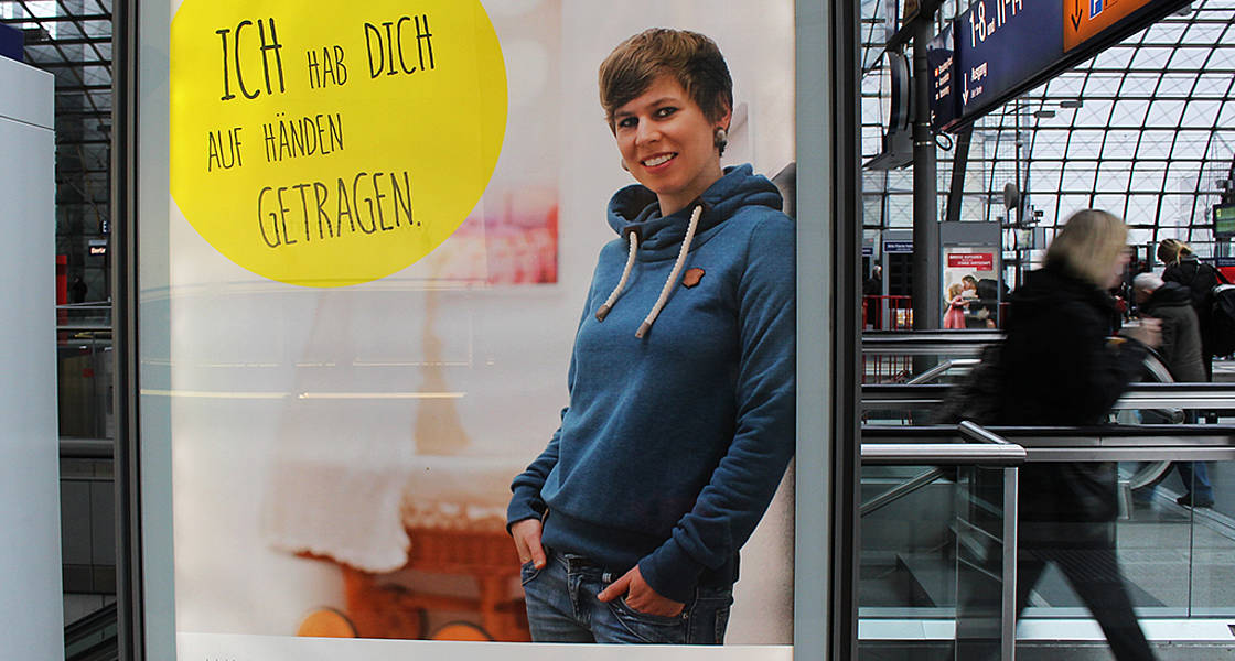 Beleuchtetes Poster mit Hebamme Lea "Ich habe dich auf Hönden getragen" am Hauptbahnhof Berlin 