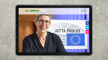 Ein Tablet, auf dem die Website von Jutta Paulus zu sehen ist. Sie zeigt ein Bild der Parlamentarierin.