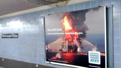 18-1_BEE_Weinmeister Bild einer brenenenden Ölplattform in einer U-Bahn Station. Über dem Poster ist ein schwarzer Fleck an der Decke