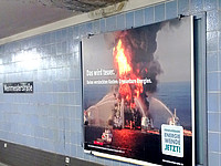 Bild einer brenenenden Ölplattform in einer U-Bahn Station. Über dem Poster ist ein schwarzer Fleck an der Decke