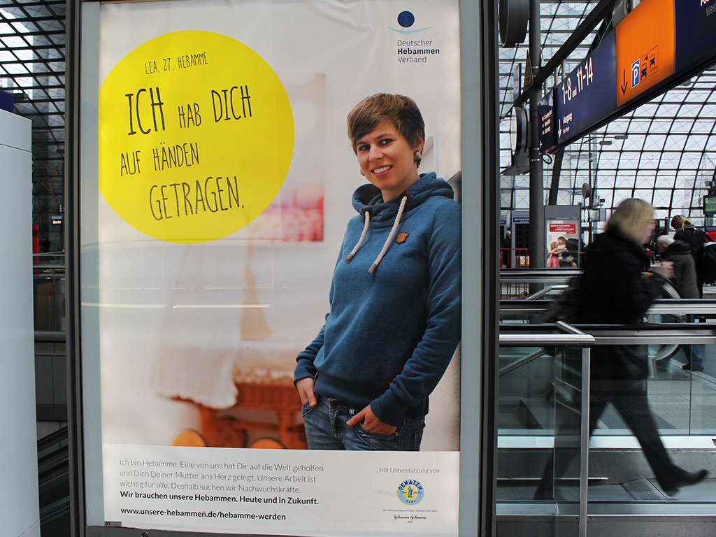 CLP Hauptbahnhof Beleuchtetes Poster mit Hebamme Lea "Ich habe dich auf Hönden getragen" am Hauptbahnhof Berlin